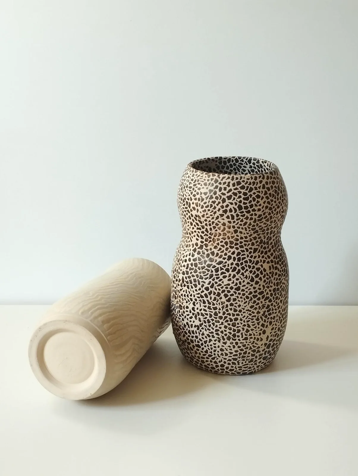 Two stoneware vessels — a cream piece and a black crackle-glazed piece